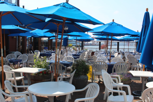 Patio set up with tables and blue umbrellas for restaurant on a pier on the waterfront in Summer in Seattle, Washington.