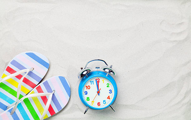 Colorful flip flops and classic alarm clock Colorful flip flops and classic alarm clock on white sand. Photo with high angle view. odessa beach stock pictures, royalty-free photos & images