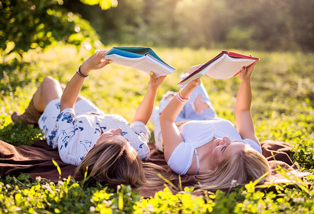 Two female college students lying at the park and studying from books.