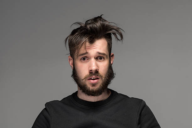 Portrait of young tousled man in studio Portrait of young tousled man with a beard and mustache in studio on gray background men hair cut stock pictures, royalty-free photos & images