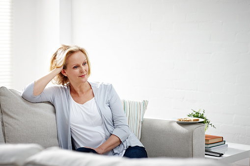 Indoor shot of mature woman sitting on sofa and thinking