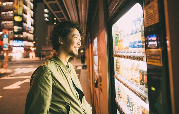 Young japanese man buys drink from the machine Young japanese man buys drink from the machine during the night and smile. The drink machine is on the street and there is nobody on the street. vending machine photos stock pictures, royalty-free photos & images