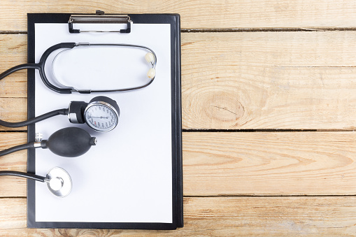 Medical clipboard and stethoscope on wooden desk background. Top view. Workplace of a doctor.