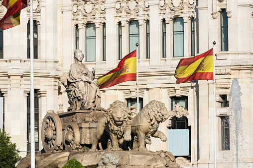 Cibeles fountain in Madrid surrounded by Spanish flags, a neoclassical marble sculpture that has become an icon of the city.