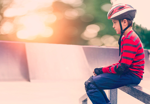 Little boy sitting in rollerblades and helmet on a bench.