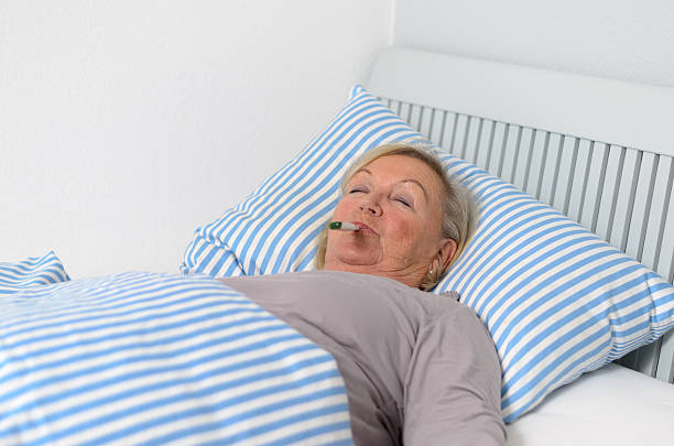 istock Sick Woman Lying on Bed with Thermometer in Mouth 476777008