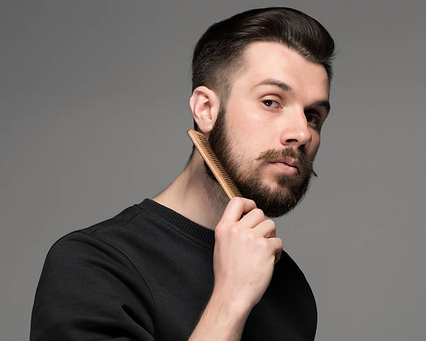 young man comb his beard and moustache young man comb his beard and moustache on gray background stubble stock pictures, royalty-free photos & images