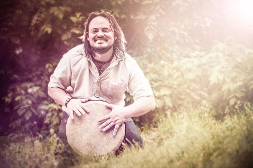 A stock photo of a man playing a beautiful hand drum in the woods on a summer afternoon