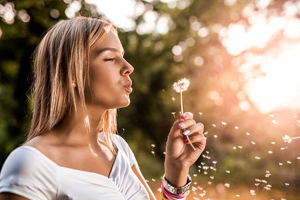 istock Young beautiful woman blowing dandelion at sunset. 476792654