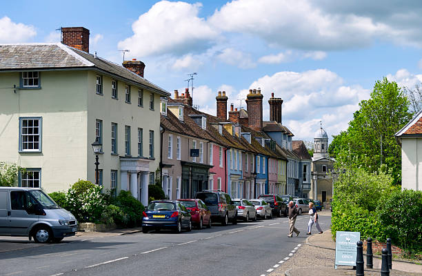 Mistley, Essex, England - May 13, 2015: Colourful old houses in Mistley High Street, Essex, eastern England, with two people crossing the road. In the distance, just visible, is one of the towers of ‘Mistley Towers’ - all that is left of a former church. Mistley is an attractive little town on the River Stour.