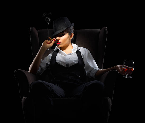 Young woman with cigar and brandy glass on chair Young woman with cigar and brandy glass on chair isolated smoking women luxury cigar stock pictures, royalty-free photos & images