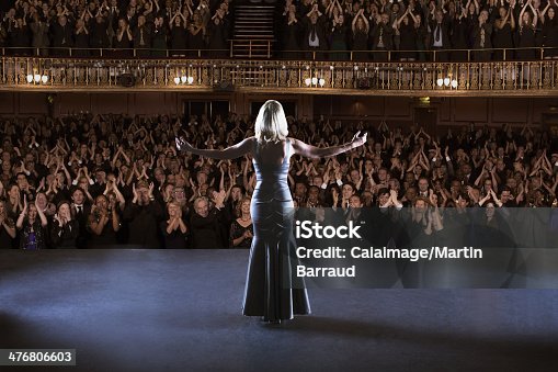 istock Performer standing with arms outstretched on stage in theater 476806603