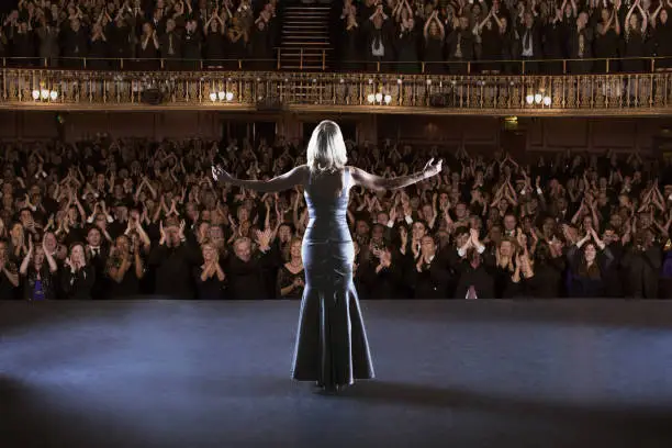 Photo of Performer standing with arms outstretched on stage in theater