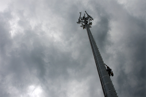 Belmont, North Carolina, USA - June 17, 2013: A tower construction worker makes his way down from the top of a Communications Tower to avoid an approaching thunderstorm. Workers hang from safety belts and cages over ten stories high to hang communications components to the tower. Presently, there are over 150,000 communications towers constructed in the United States.