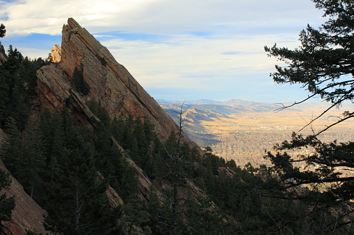 A view looking north of the Colorado Flatirons, located in Boulder, Colorado. This photo was taken at the climax of a hike that reached the top of an adjacent flatiron. The view north shows brown fields and foothills stretching up the front range. Photo taken in February, before any springtime growth. Colors of blue, brown, green.