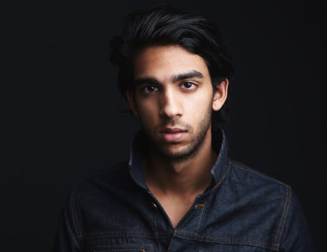 Front portrait of a young man with denim jeans jacket posing against dark background