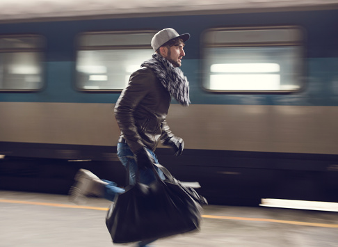 Young man running at railroad station and trying to catch the train. Blurred motion.