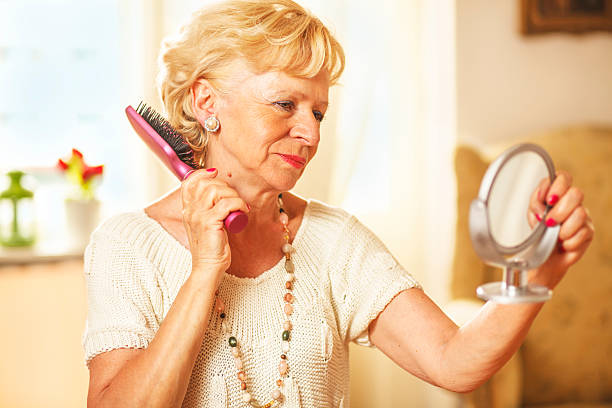 istock Smiling elderly woman comb hair and looked in the mirror 476835634