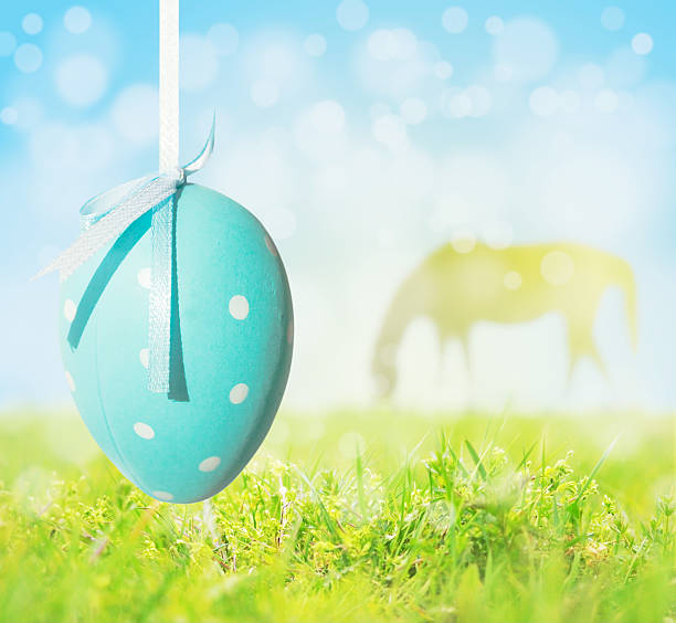 Easter egg hanging on background of grass, sky, grazing horse stock photo
