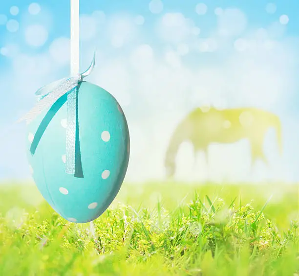 Photo of Easter egg hanging on background of grass, sky, grazing horse