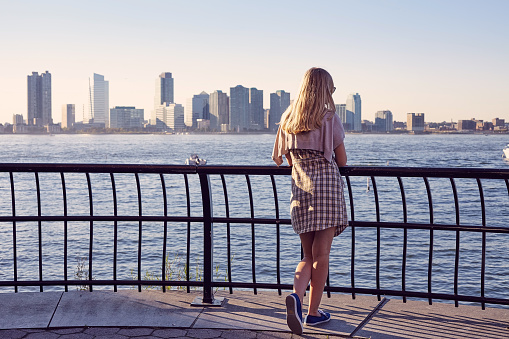 Back view of blonde young woman leaning on berth railing in port on sunny summer day