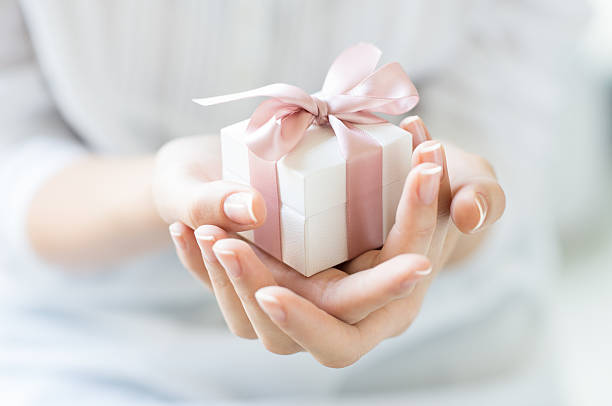 Romantic gift box Close up shot of female hands holding a small gift wrapped with pink ribbon. Small gift in the hands of a woman indoor. Shallow depth of field with focus on the little box. hand holding gift stock pictures, royalty-free photos & images