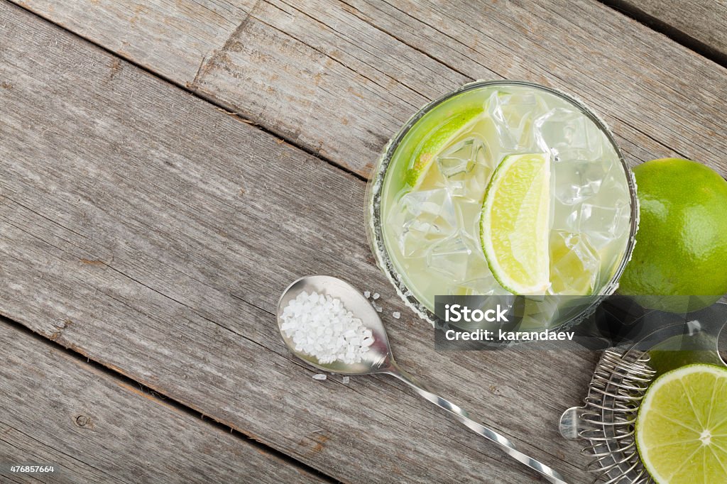 Classic margarita cocktail with salty rim Classic margarita cocktail with salty rim on wooden table with limes and drink utensils Margarita Stock Photo