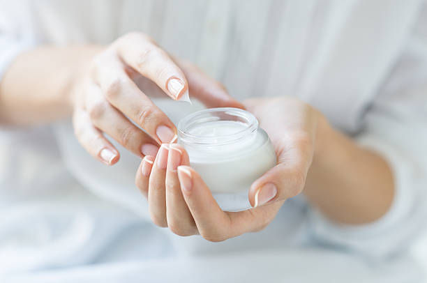Beautiful woman hands applying moisturizer Closeup shot of hands applying moisturizer. Beauty woman holding a glass jar of skin cream. Shallow depth of field with focus on moisturizer. antiaging stock pictures, royalty-free photos & images