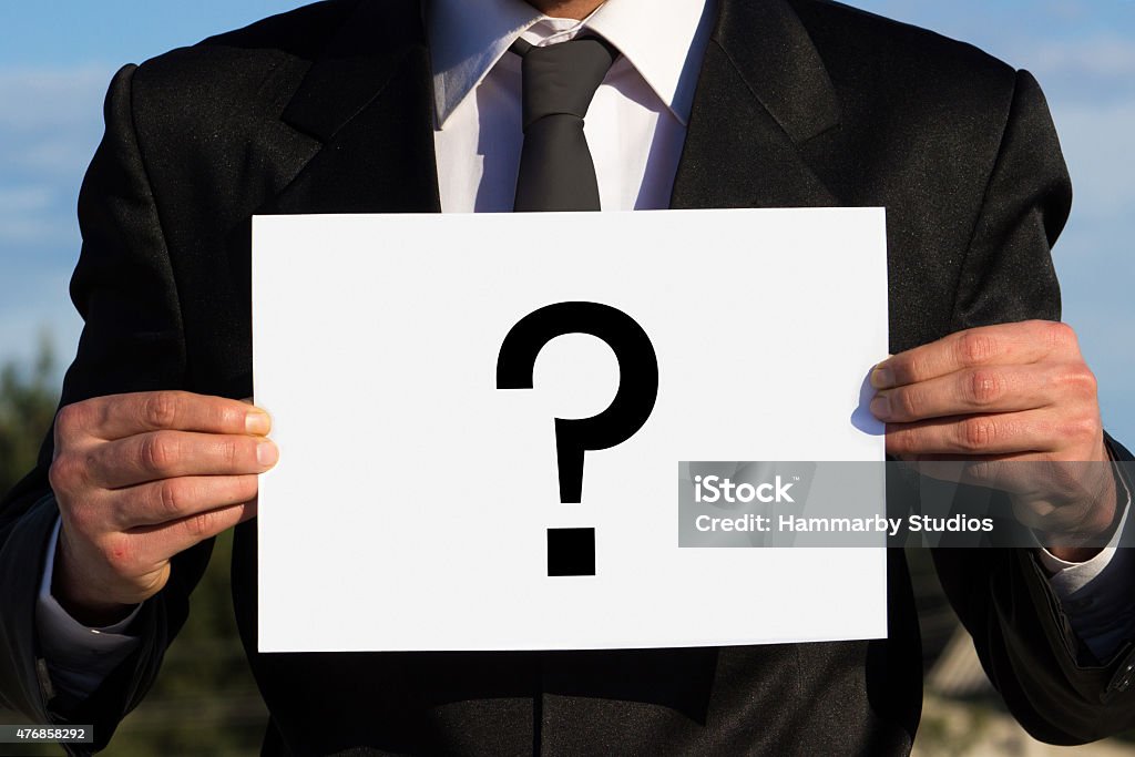 Unrecognizable businessman holding a question mark on poster Unrecognizable businessman holding a question mark on poster. Man wearing black suit. Image developed from Raw. Focus on businessman. Business Stock Photo