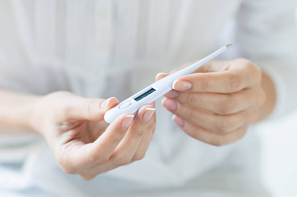 Woman looking at thermometer Closeup shot of a woman looking at thermometer. Female hands holding a digital thermometer. Girl measures the temperature. Shallow depth of field with focus on thermometer. fever stock pictures, royalty-free photos & images