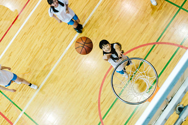 Japanese high school. A school gymnasium. Children play basketball A view of a Japanese high school. A school sports hall with court markings. Children practice their basketball skills with one child shooting directly into the shot. Interior, horizontal composition. Light reflected on the highly polished floor. youth basketball indoor stock pictures, royalty-free photos & images