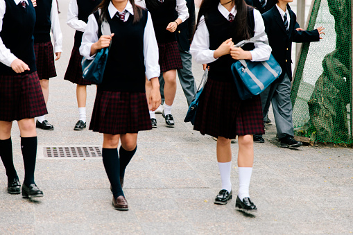 Students wearing school uniform, leaving school for the day in Gateshead, North East England. They are talking to each other while walking out of the building.