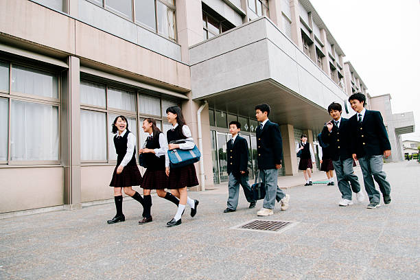 A view of a Japanese high school. A group of young students walk together outside in their school playground. Exterior, smiling, contemporary architecture, exterior view, horizontal composition. 