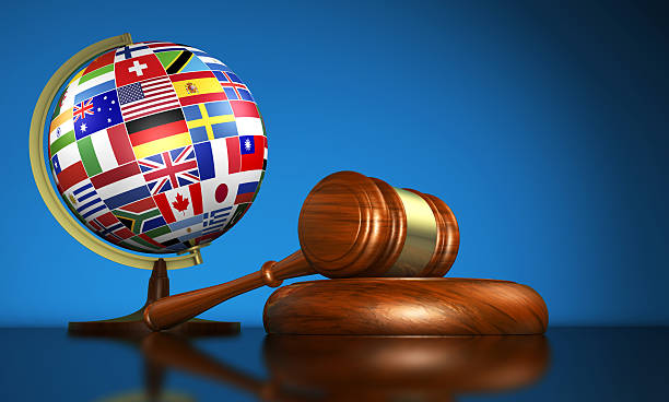 International law systems, justice, human rights and global business education concept with world flags on a school globe and a gavel on a desk on blue background.