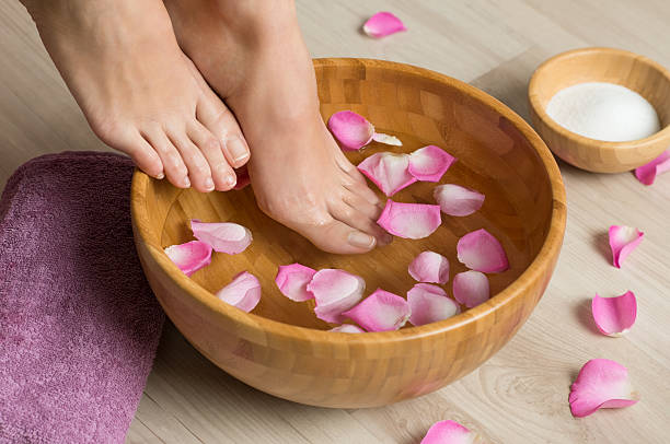Pedicure at spa center Closeup shot of a woman feet dipped in water with petals in a wooden bowl. Beautiful female feet at spa salon on pedicure procedure. Shallow depth of field with focus on feet. foot spa treatment stock pictures, royalty-free photos & images