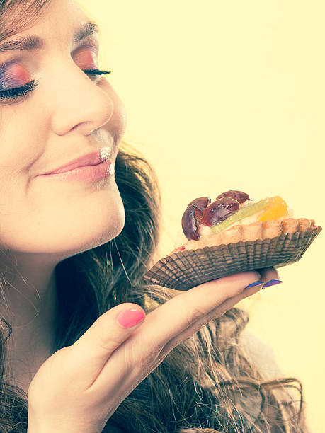 woman closed eyes holds cake in hand Bakery sweet food indulging and people concept. Cute attractive woman closed eyes holds cake cupcake in hand smelling yellow background gir forest national park stock pictures, royalty-free photos & images