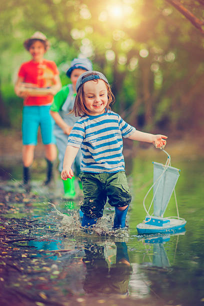 Little boys and girl with  toy ship near a lake in summer