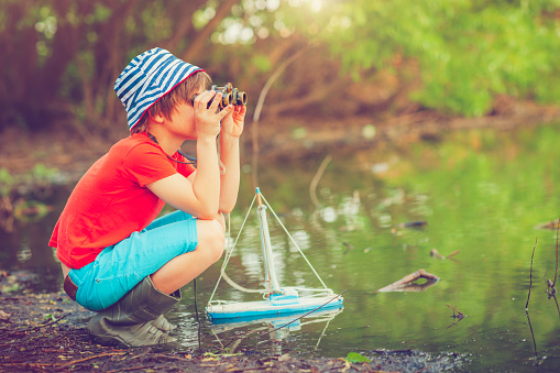 Little boy with his toy ship near a lake in summer