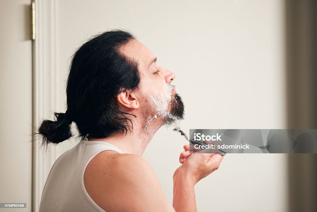 Man Shaving Beard A profile view of a man shaving off his beard with a razor. Shaving Stock Photo