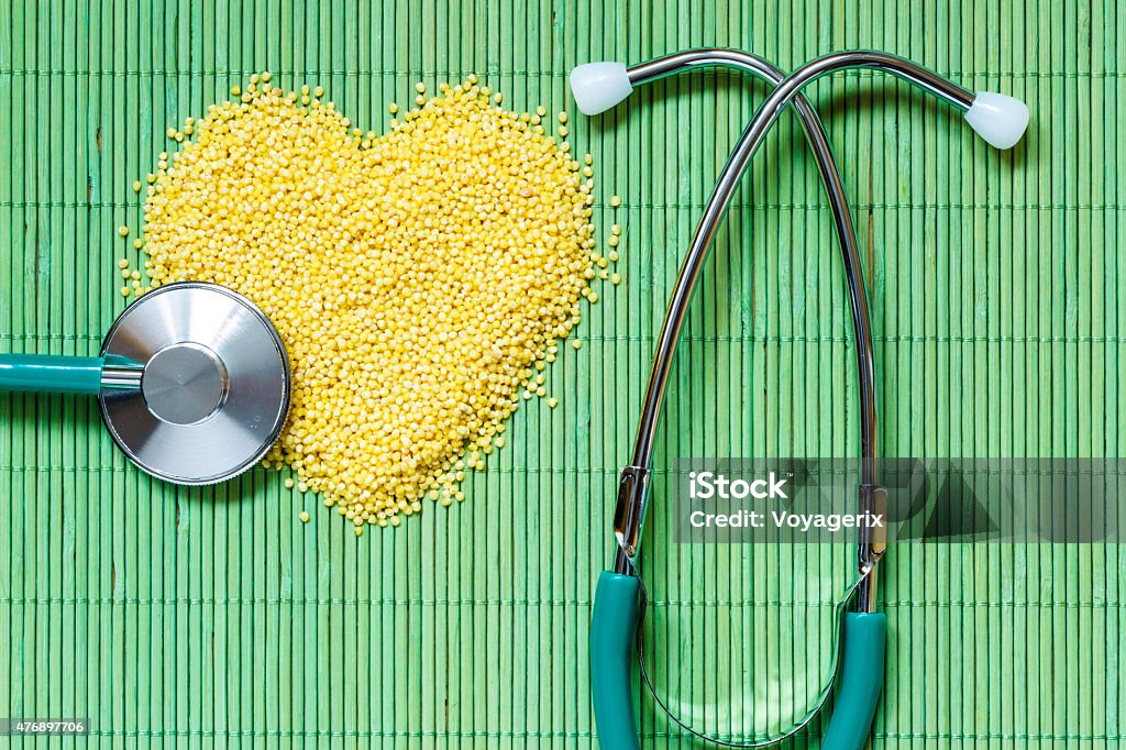 Millet groats heart shaped on green mat surface. Dieting healthy living concept. Millet groats heart shaped and stethoscope on green mat surface.. Healthy food help lower cholesterol. 2015 Stock Photo