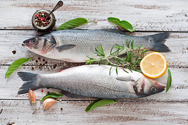 Two raw seabass with spices on an old wooden background. Two raw seabass with spices on an old wooden background. catch of fish stock pictures, royalty-free photos & images
