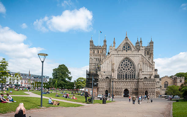Tourists Relaxing In The Gardens Around A Cathedral Exeter, United Kingdom - May 26, 2015: Tourists and pedestrians relaxing in the gardens around Exeter Cathedral grounds. Exeter Cathedral is an Anglican cathedral dating back to 1050. anglican stock pictures, royalty-free photos & images