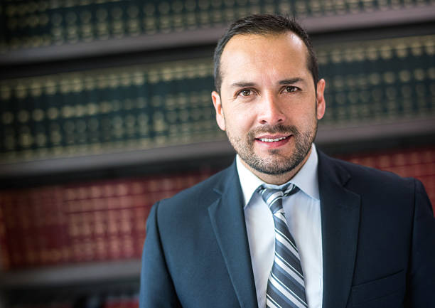 A male lawyer or a businessman carrying a briefcase looks into the distance as he stands along a row of Greek columns that could represent a financial, leagal, or higher learning institution.