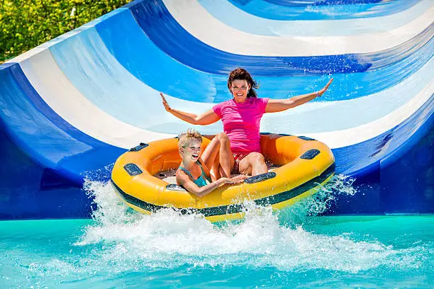 Child with mother on water slide at aquapark. Two persons on summer holiday.