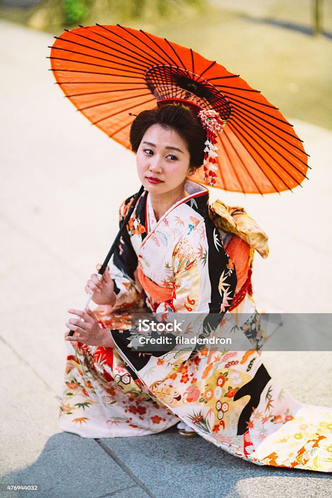 Japanese woman with oil paper umbrella Beautiful japanese woman stand on the floor outside during a lovely sunny day. She wears kimono, obi and hold oil paper umbrella.The kimono is very colorful and elegant. She seems very pensive. There is beautiful kanzashi in her hair. Furisode Stock Photo