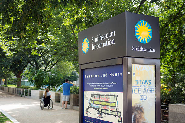 Sign of Smithsonian Institute in Washington, DC Washington, United States - August 18, 2014: People meander about the pathway outside the Smithsonian National Museum of Natural History along the National Mall behind a sign and kiosk displaying information for the museum. With free admission and open doors 364 days a year, the museum is the second most visited museum in the world, the most visited natural history museum in the world, and the most visited museum (of any type) in North America. smithsonian museums stock pictures, royalty-free photos & images