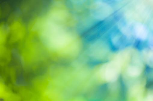 Natural outdoors bokeh background in green and blue tones with sun rays
