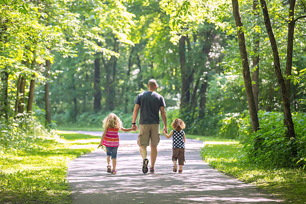 Father And Two Daughters Walking Through Woods at Park stock photo