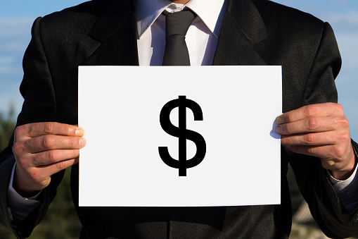 Businessman holding a Dollar sign. Unrecognizable person. Man wearing black suit. Outdoors shot. Horizontal composition. Image developed from Raw format.