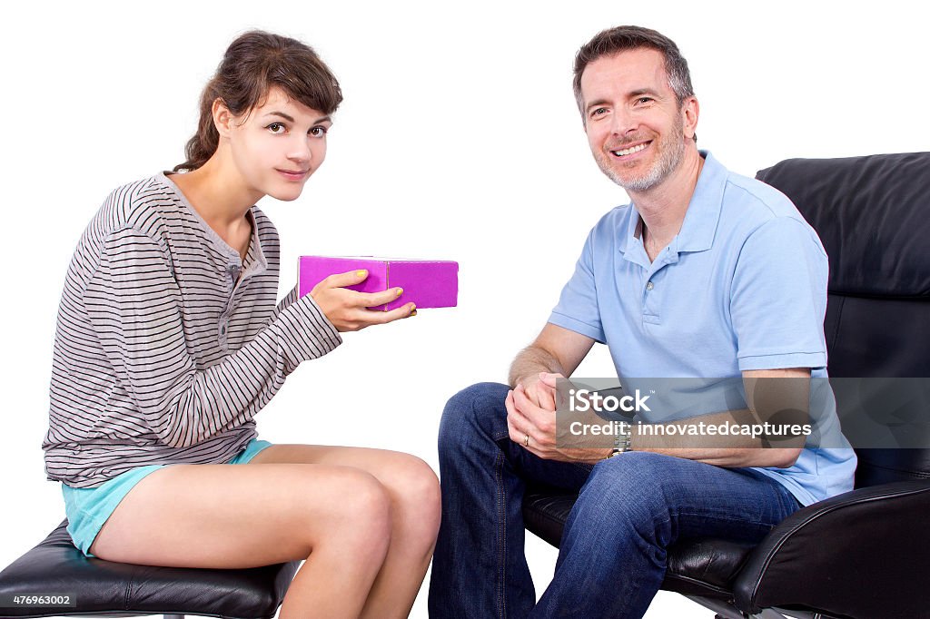 Daughter Giving a Fathers Day Gift Teenage daughter giving a surprise gift to her single father.  The dad is sitting on a chair while she is giving him a purple package.  The gift is either a Father's Day gift, Christmas gift, or a birthday gift.  They are isolated on a white background. 2015 Stock Photo